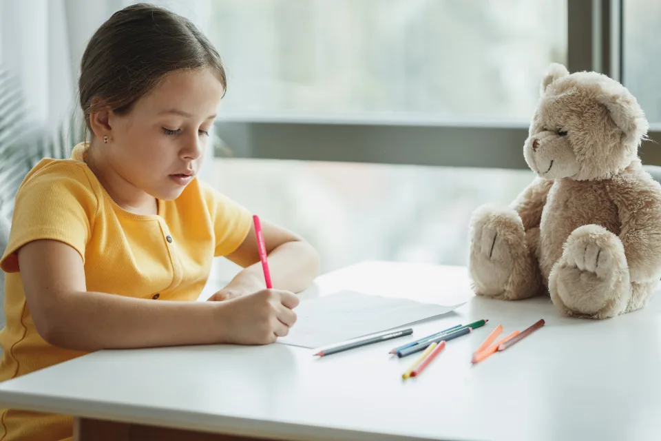 Una alumna escribe concentrada con lápices de colores en un aula luminosa.