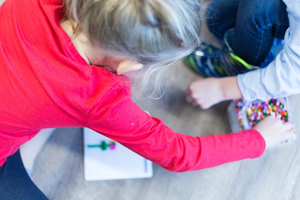 Dos niños de preescolar juegan y construyen con un material didáctico de colores en el piso del aula.