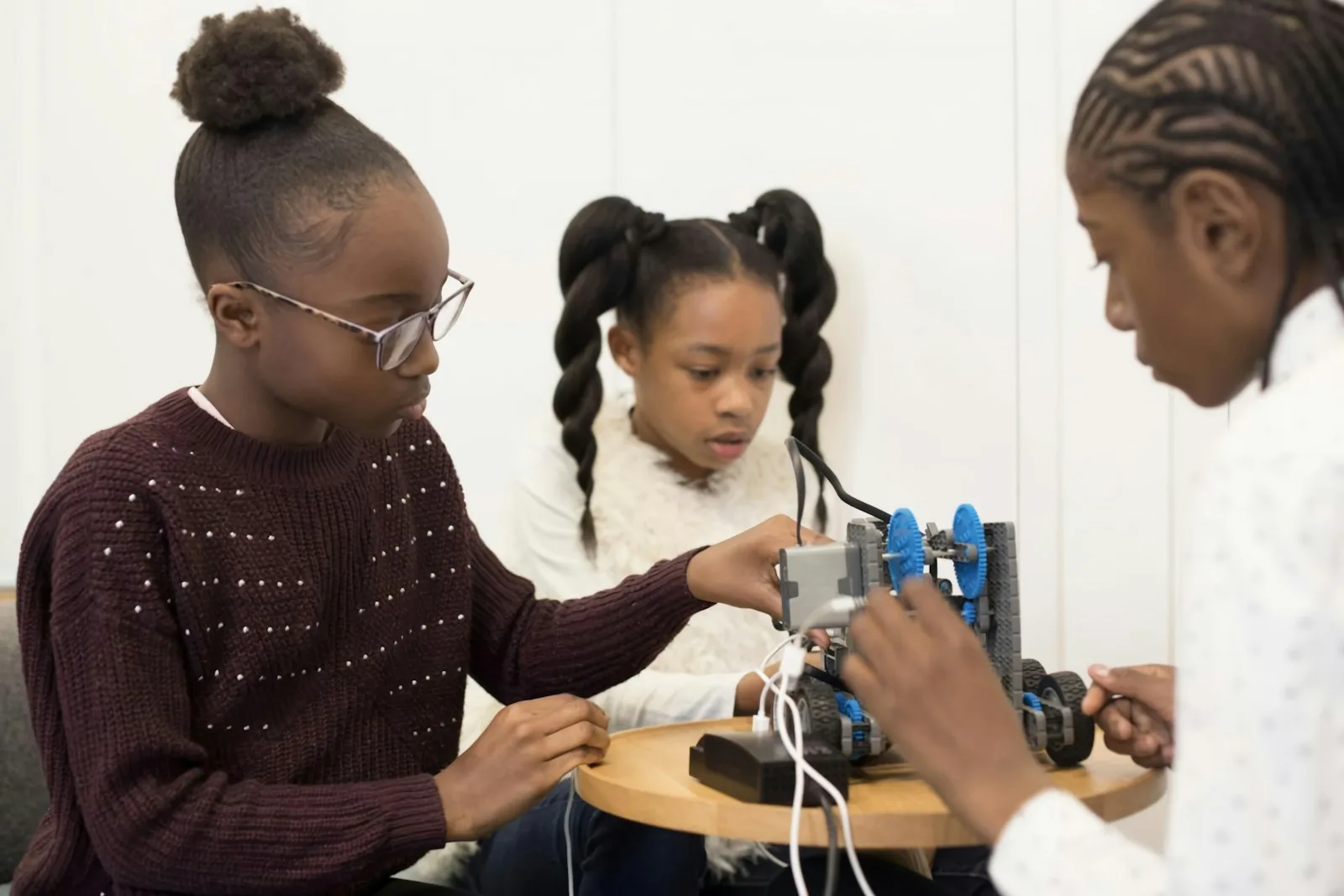 Three students wiring a motorized robot together at a workshop table