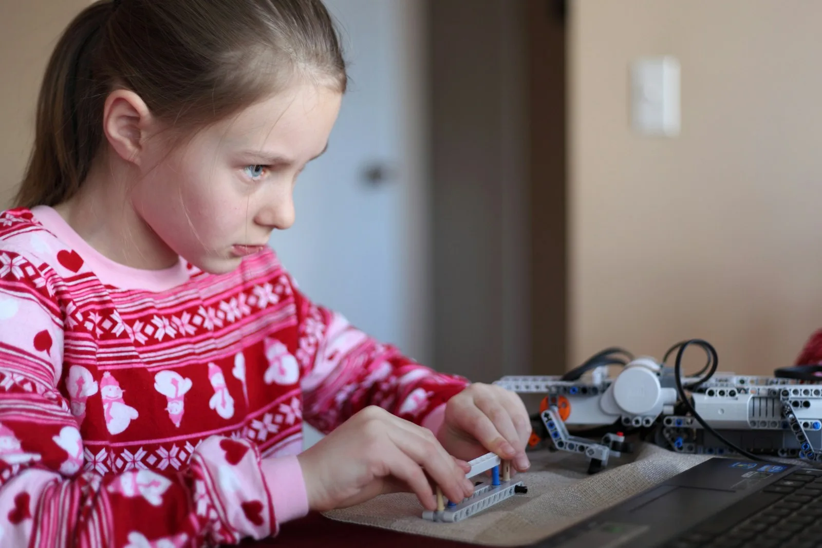 A girl concentrating as she assembles a programmable robotics kit beside a laptop