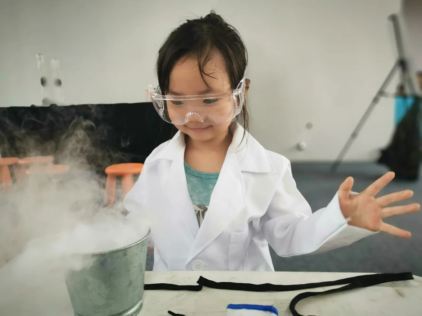 A young scientist in lab coat and goggles running an experiment with rising vapor