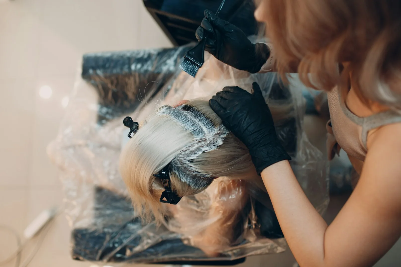 Overhead view of a colorist hand-painting lightener across sectioned blonde hair.